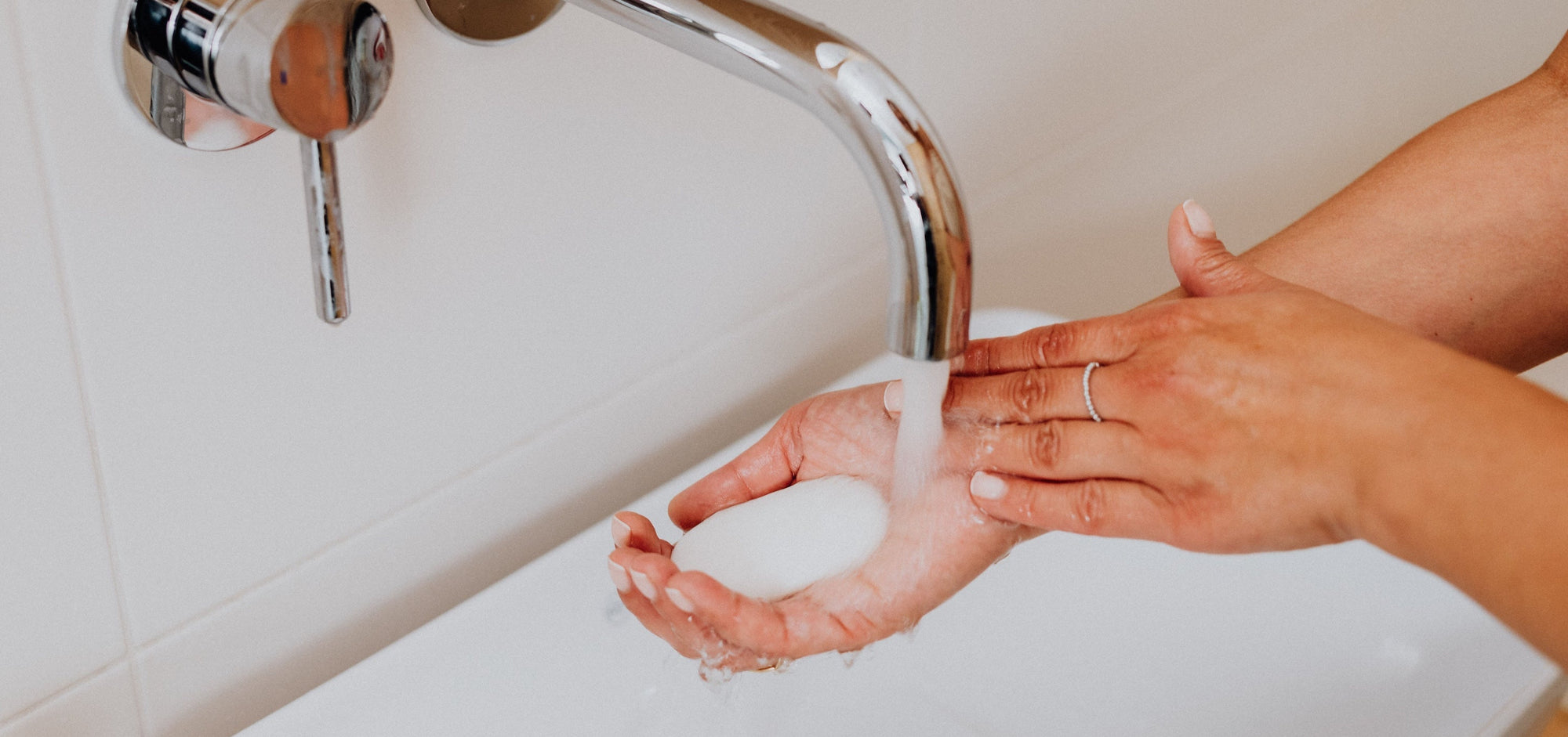 Person washing hands under a faucet in a bathroom setting